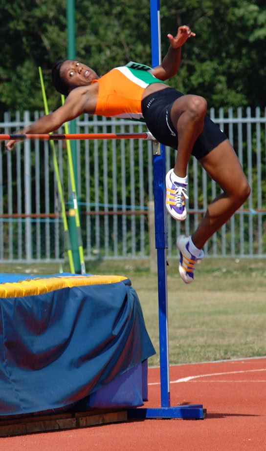 Athlete in mid-air performing a high jump over a bar on an outdoor track and field competition.